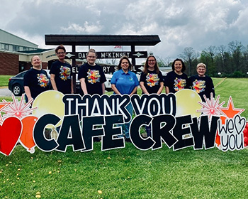adults behind a sign that reads Thank you cafe crew