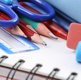 Pencils, pens, erasers, scissors and a ruler on top of a notebook